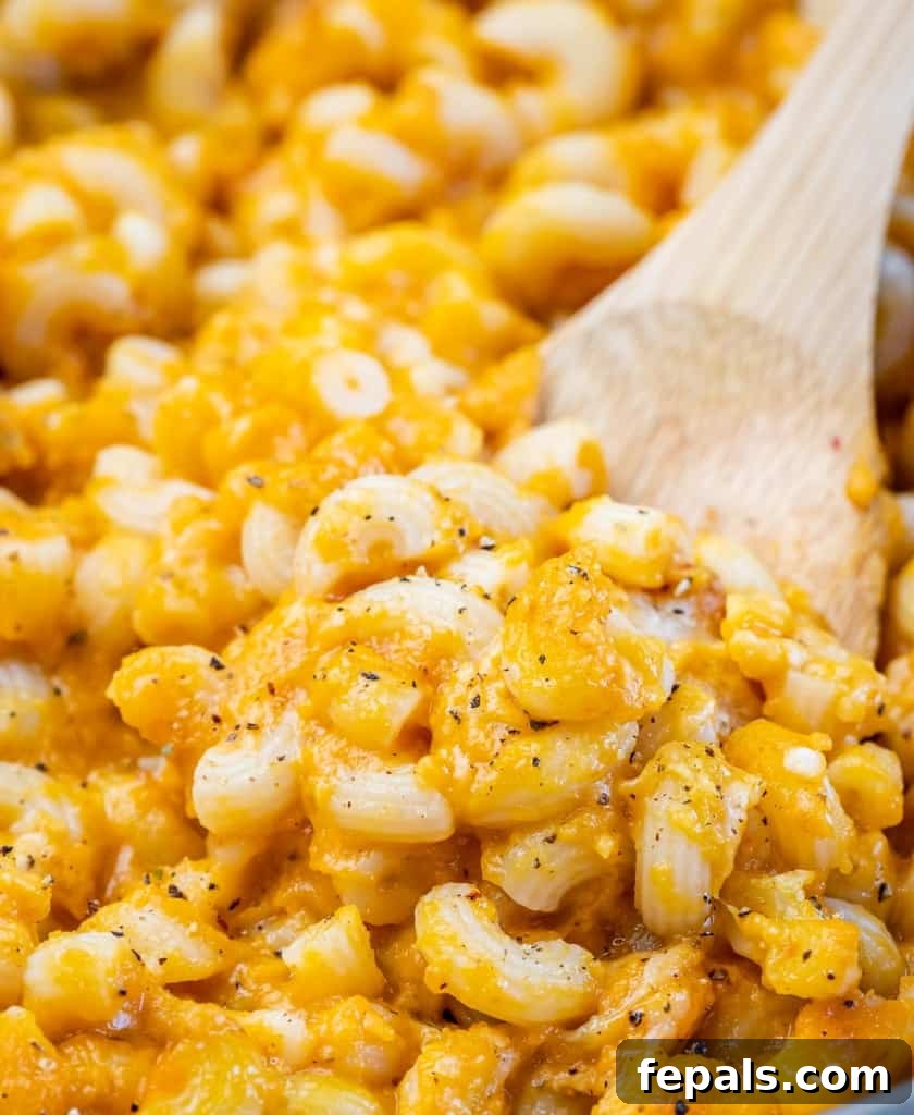 Roasted Pumpkin Mac and Cheese 3 Wooden spoon stirring cheesy pasta shells.