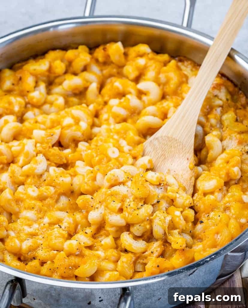 Roasted Pumpkin Mac and Cheese 10 Stirring pumpkin Mac and cheese with a wooden spoon in a pot.