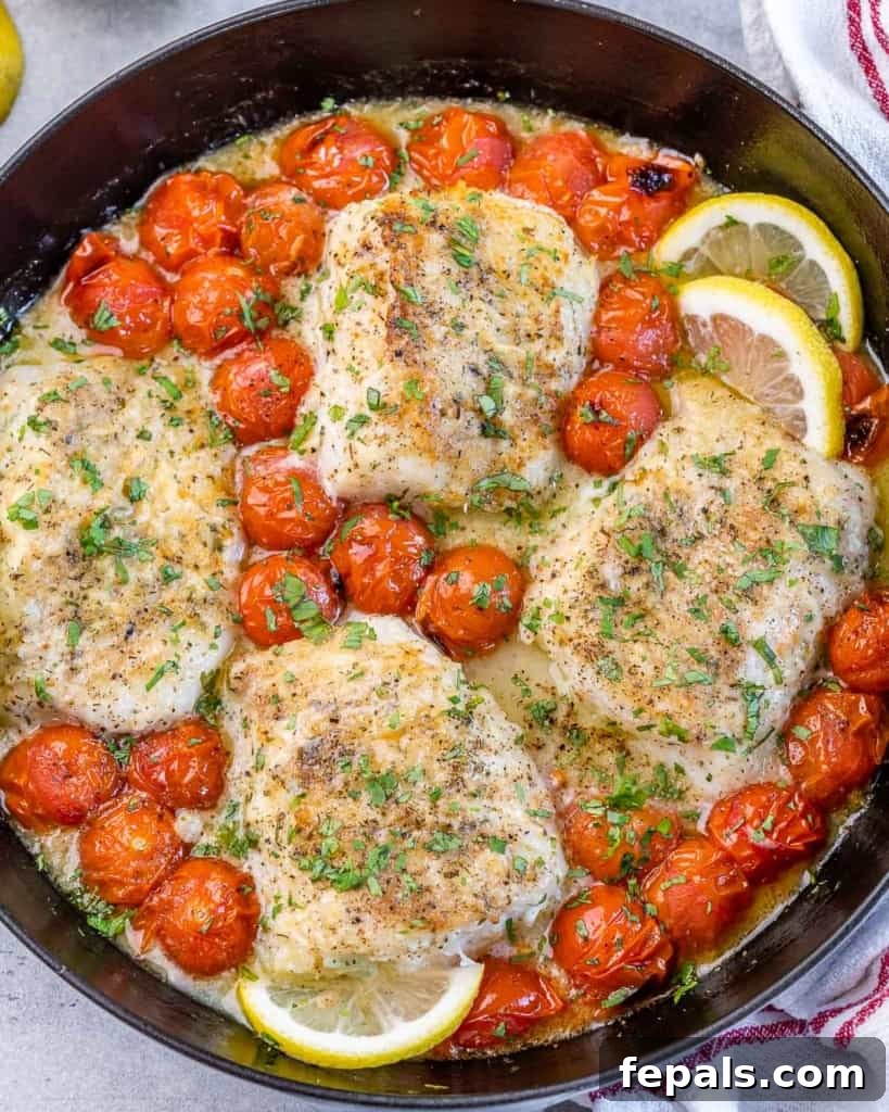Bright Lemon Garlic Cod Bake 2 top view of a black skillet with 4 baked cod fillets and blistered cherry tomatoes along with lemon slices garnishes