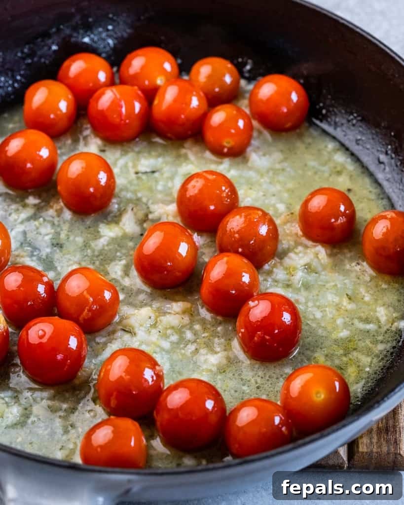 Bright Lemon Garlic Cod Bake 7 cherry tomatoes added over lemon garlic sauce on a black skillet
