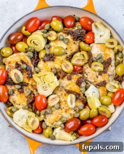 Chicken in a skillet with cherry tomatoes, artichokes and olives.