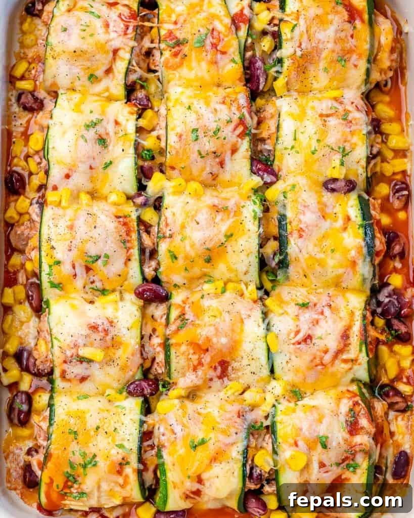 top view of chicken enchilada rolled with thinly sliced zucchini with a white dish with melted cheese on top