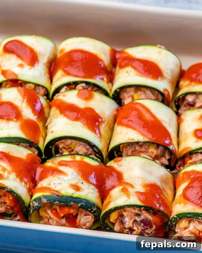chicken enchilada rolls in a baking dish assembled next to each other  topped with red sauce 