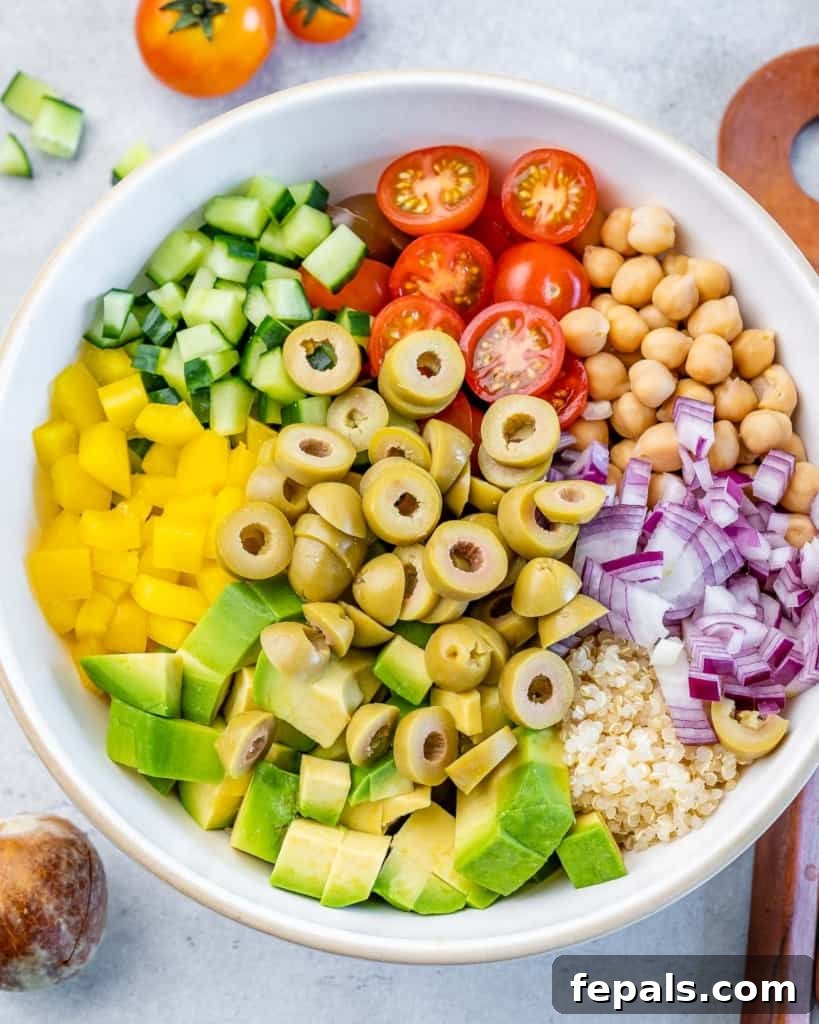 Mediterranean Chickpea Cucumber Quinoa Salad 7 Green olives, diced avocado, halved cherry tomatoes, and chopped cucumber being added to a large white salad bowl, ready for mixing.