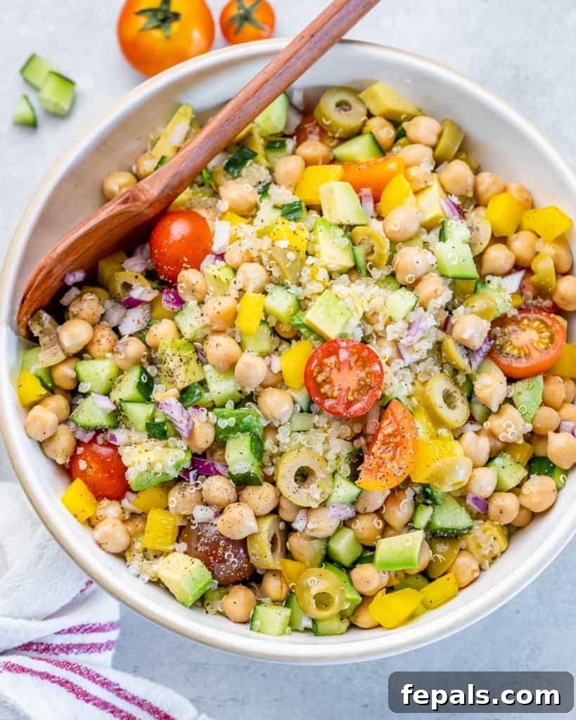 Mediterranean Chickpea Cucumber Quinoa Salad 8 A beautifully presented avocado quinoa salad served in a white bowl, with a large wooden spoon ready for serving.