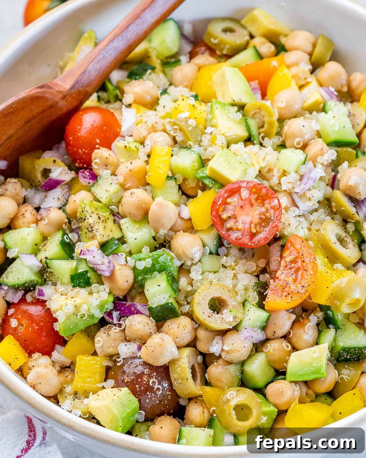 Mediterranean Chickpea Cucumber Quinoa Salad 10 A close-up view of a vibrant vegetable quinoa salad served in a white bowl with a wooden serving spoon, highlighting its fresh ingredients and textures.