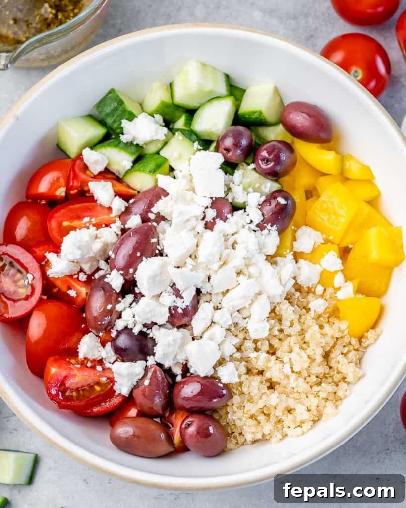 chopped veggies, quinoa, olives, and crumbled feta cheese added in a white bowl