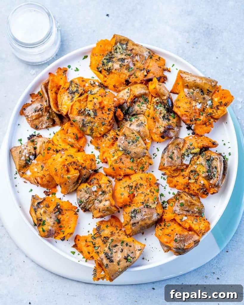 Golden Roasted Sweet Potato Smash 2 Top view of perfectly golden and crispy baked smashed sweet potatoes on a round white plate, garnished with fresh herbs.