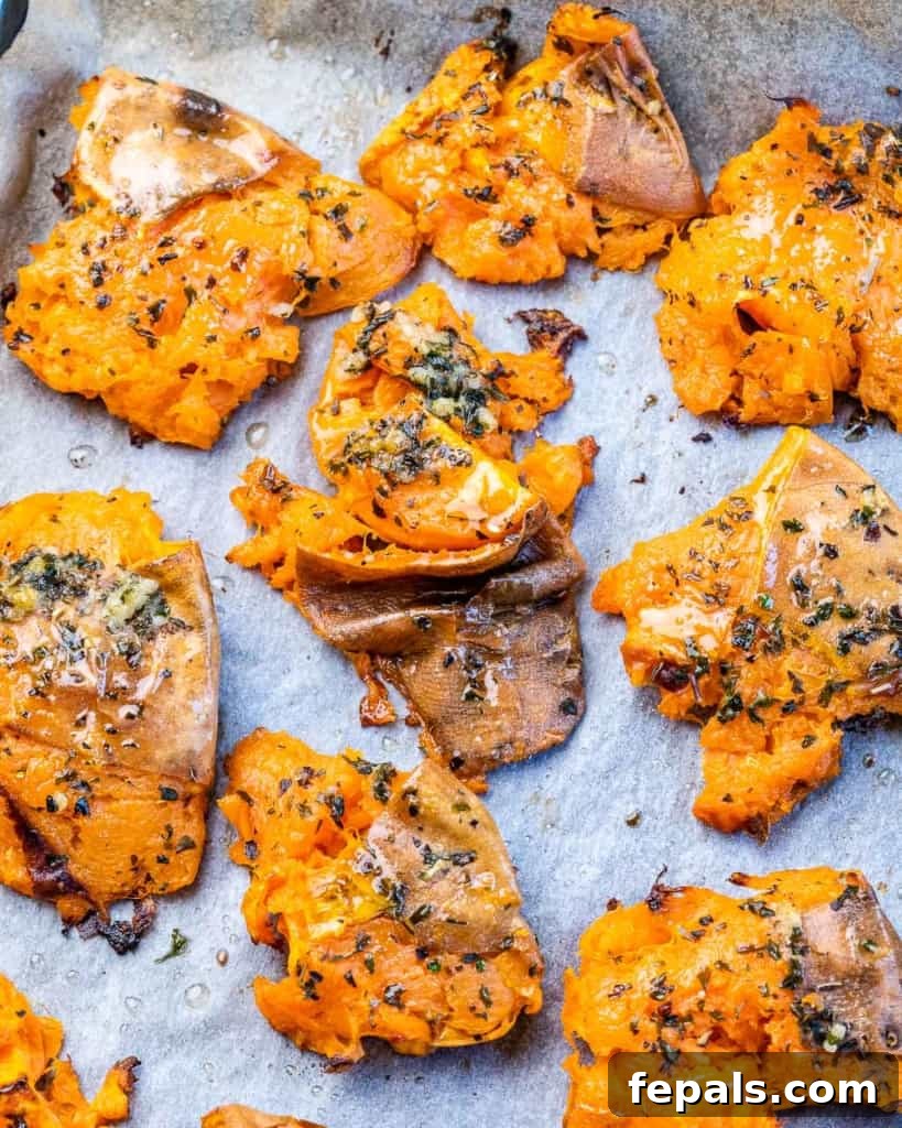 Golden Roasted Sweet Potato Smash 3 Close-up view of sweet potatoes that have been baked, smashed, and generously seasoned with a blend of fragrant dried herbs and garlic.