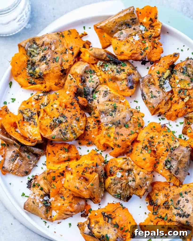 Golden Roasted Sweet Potato Smash 9 High-angle shot of a white plate piled with golden, crispy smashed sweet potatoes, showcasing their irregular, rustic edges.