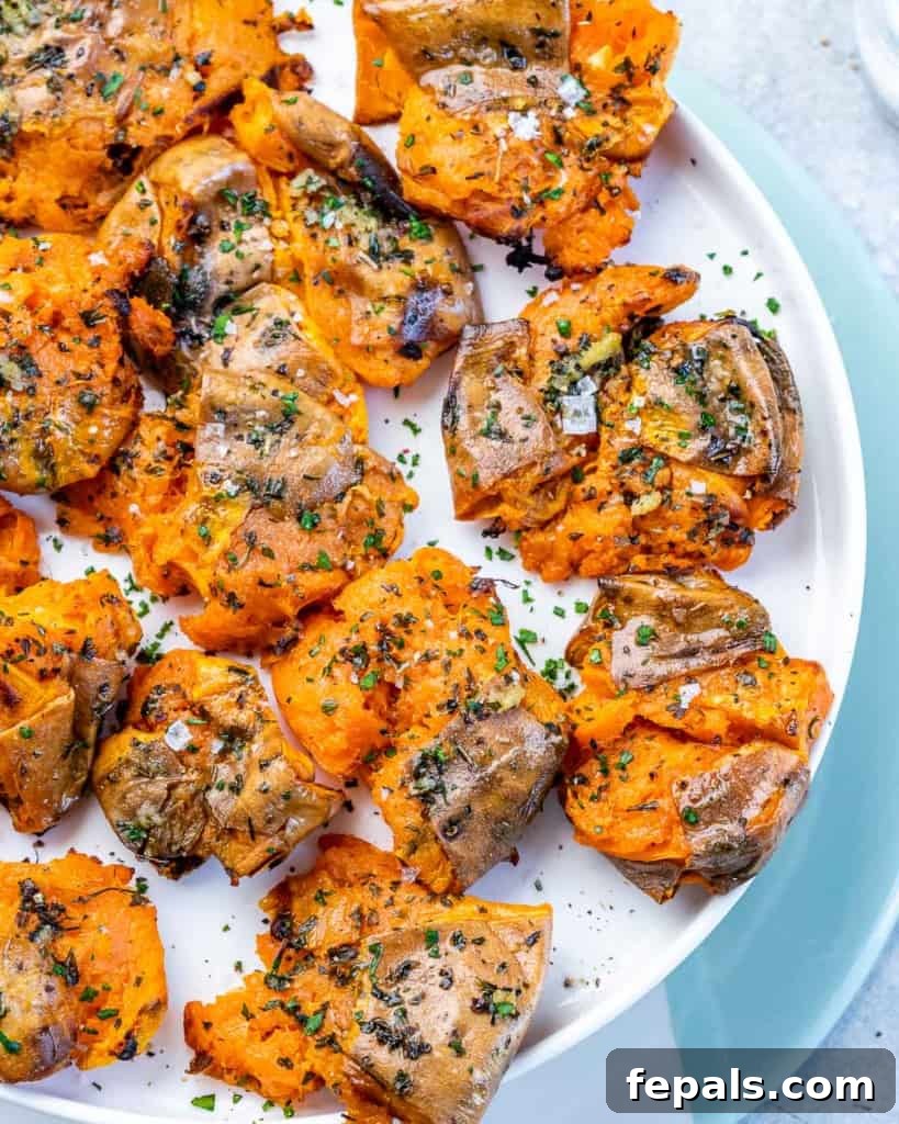 Golden Roasted Sweet Potato Smash 10 Top view of a white plate generously topped with crispy smashed sweet potatoes, garnished with fresh green herbs.