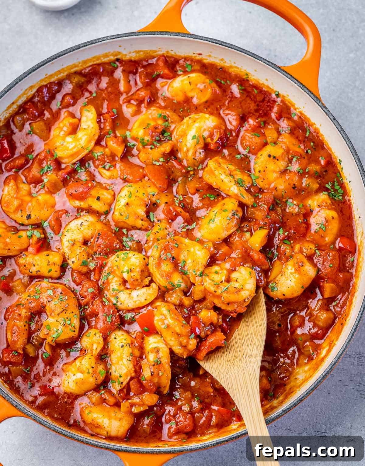 Top view creole shrimp sauté in a red tomato sauce with wooden spoon in skillet.