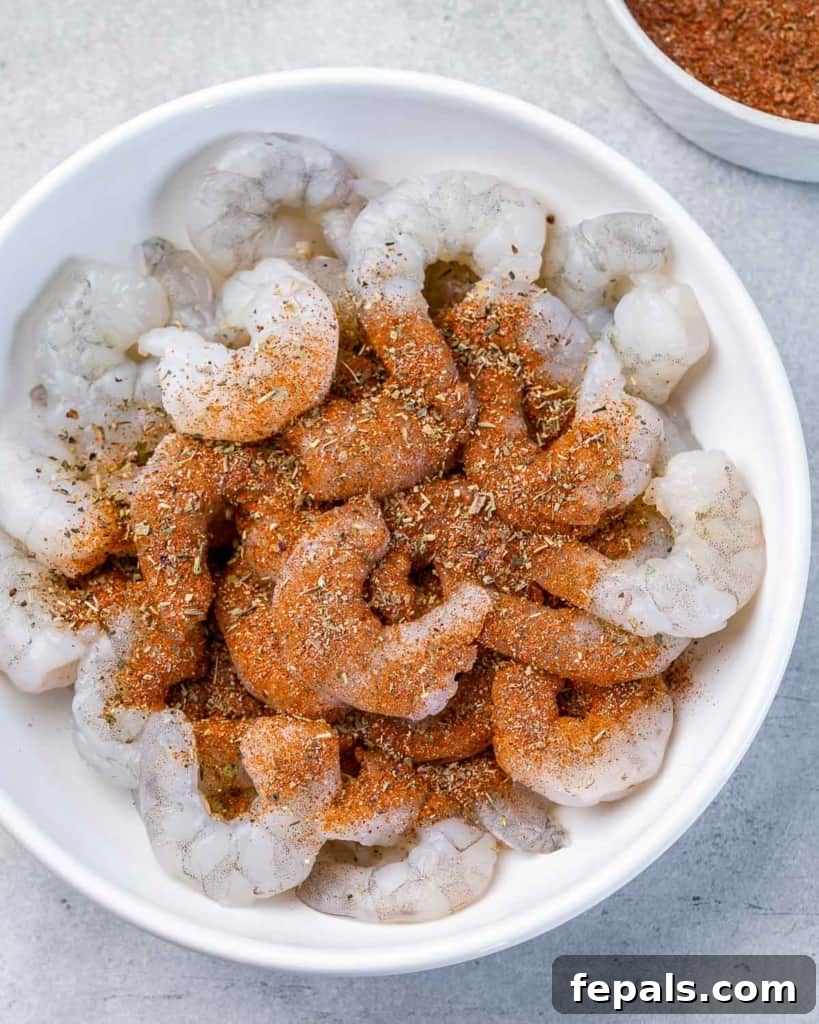Spices over uncooked shrimp in a bowl.