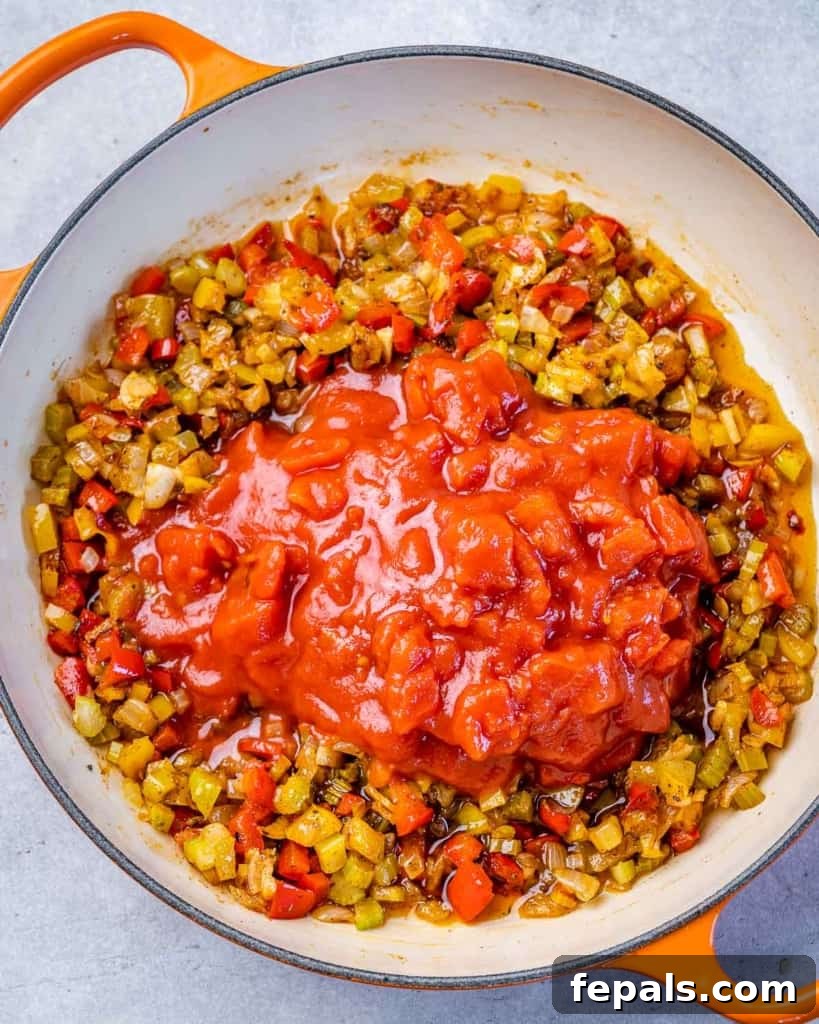 Adding tomatoes to sautéed veggies in a pot.