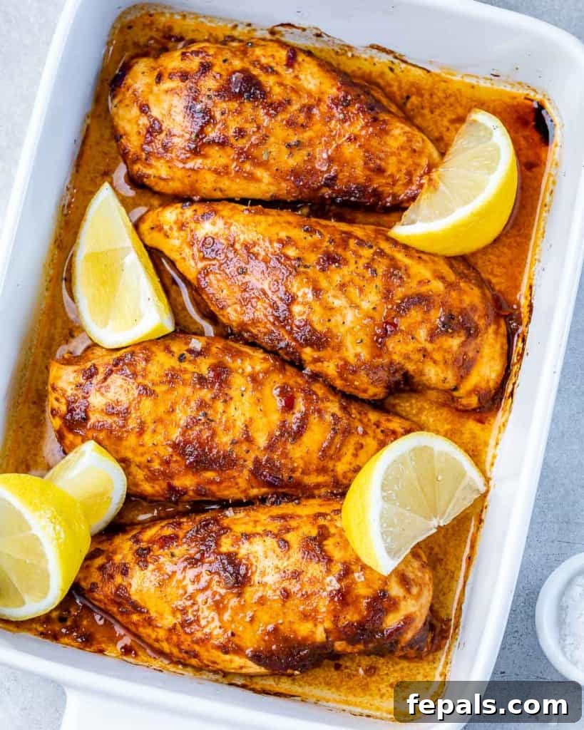 Spicy Harissa Roasted Chicken 2 top view of 4 baked chicken breasts in harissa seasonings with 4 lemon garnishes in a white baking dish