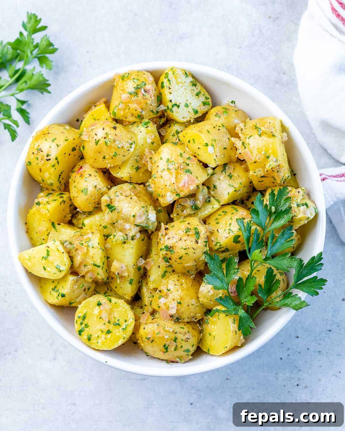 Hearty Warm German Potato Salad 2 Top view of herbed potato pieces on a white round bowl.
