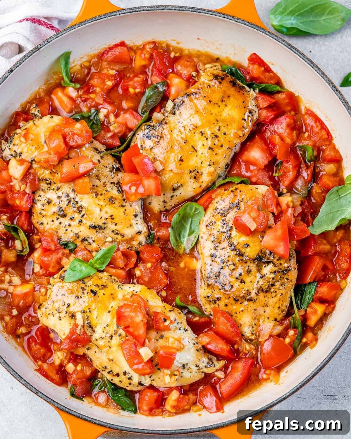 Tuscan Chicken Pomodoro 2 Top view of 4 cooked seasoned chicken breasts in a red tomato base sauce and basil garnishes on an orange skillet.