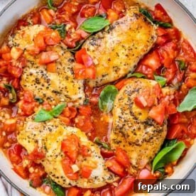 top view of 4 cooked seasoned chicken breasts in a red tomato base sauce and basil garnishes on an orange skillet