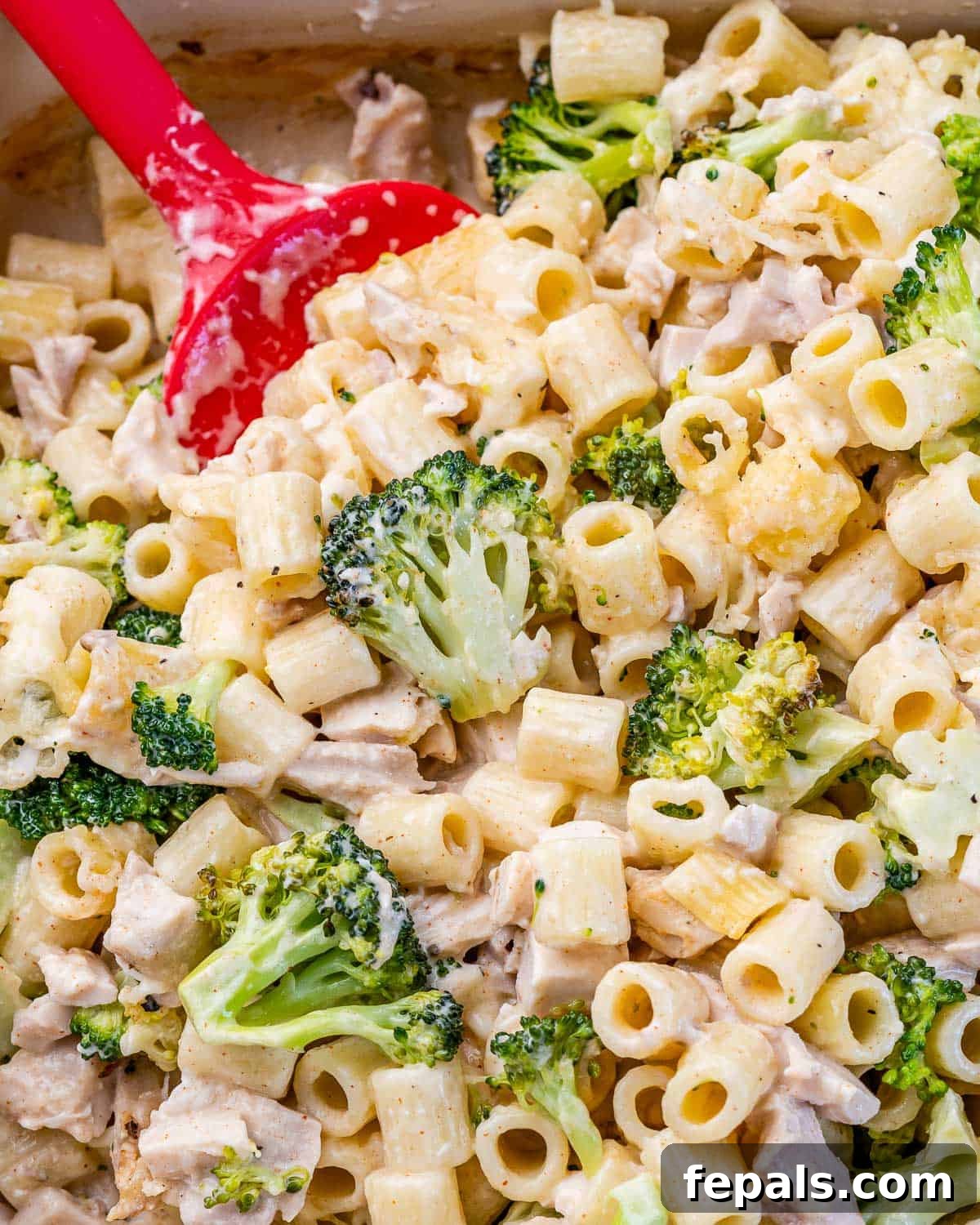Dishing out a serving of pasta, broccoli and chicken casserole from a white baking dish.