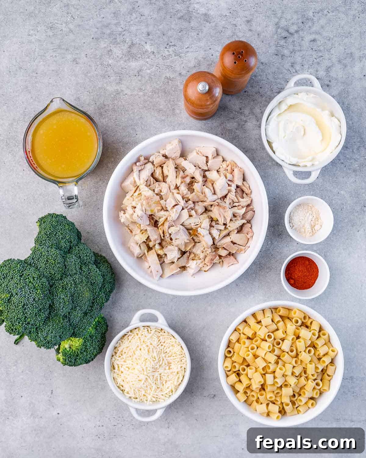Diced chicken, broccoli florets, dry pasta, chicken stock, cream cheese, and spices laid out on a table as ingredients.