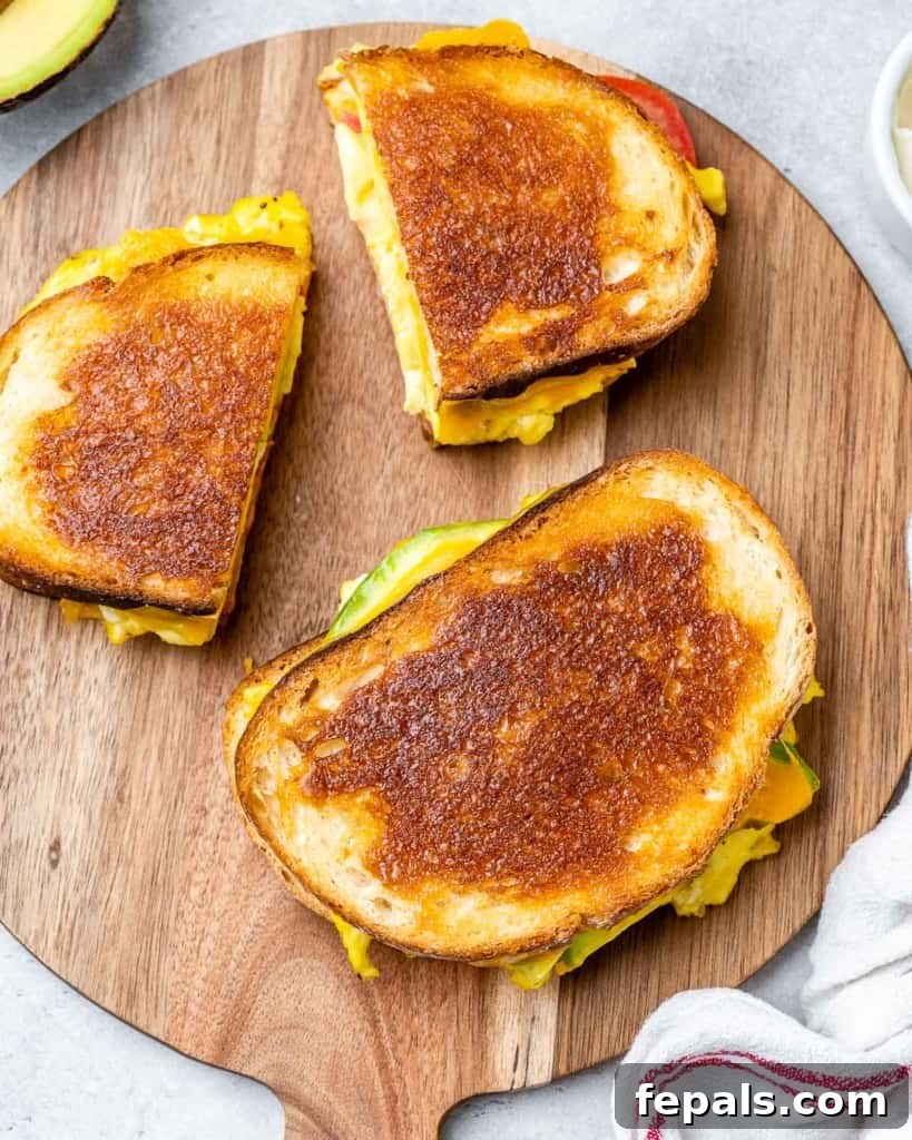 Freshly toasted breakfast egg sandwich halves arranged on a wooden cutting board, with visible melted cheese and crispy bread.