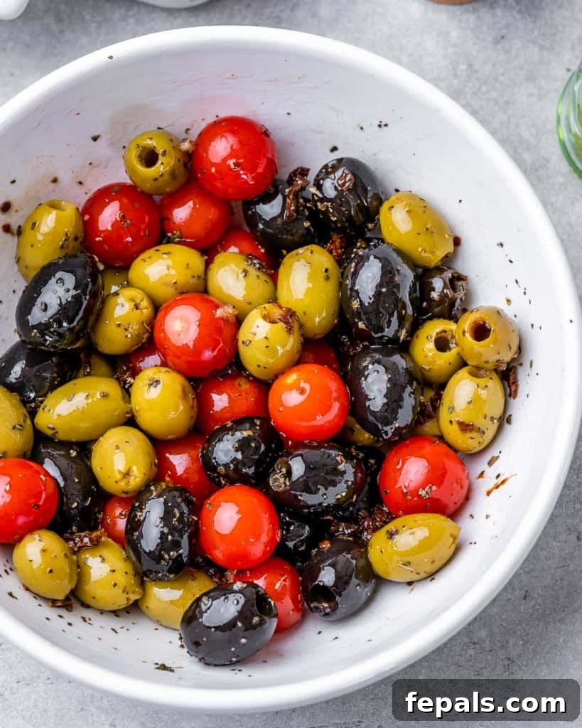 a bowl with olives and tomatoes tossed with oil and seasoning, showing the mixture before baking