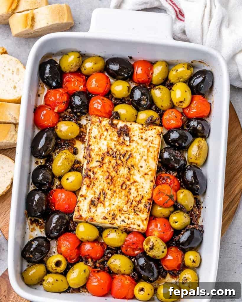 top view dish with baked feta cheese, olives, and tomatoes, garnished with fresh herbs