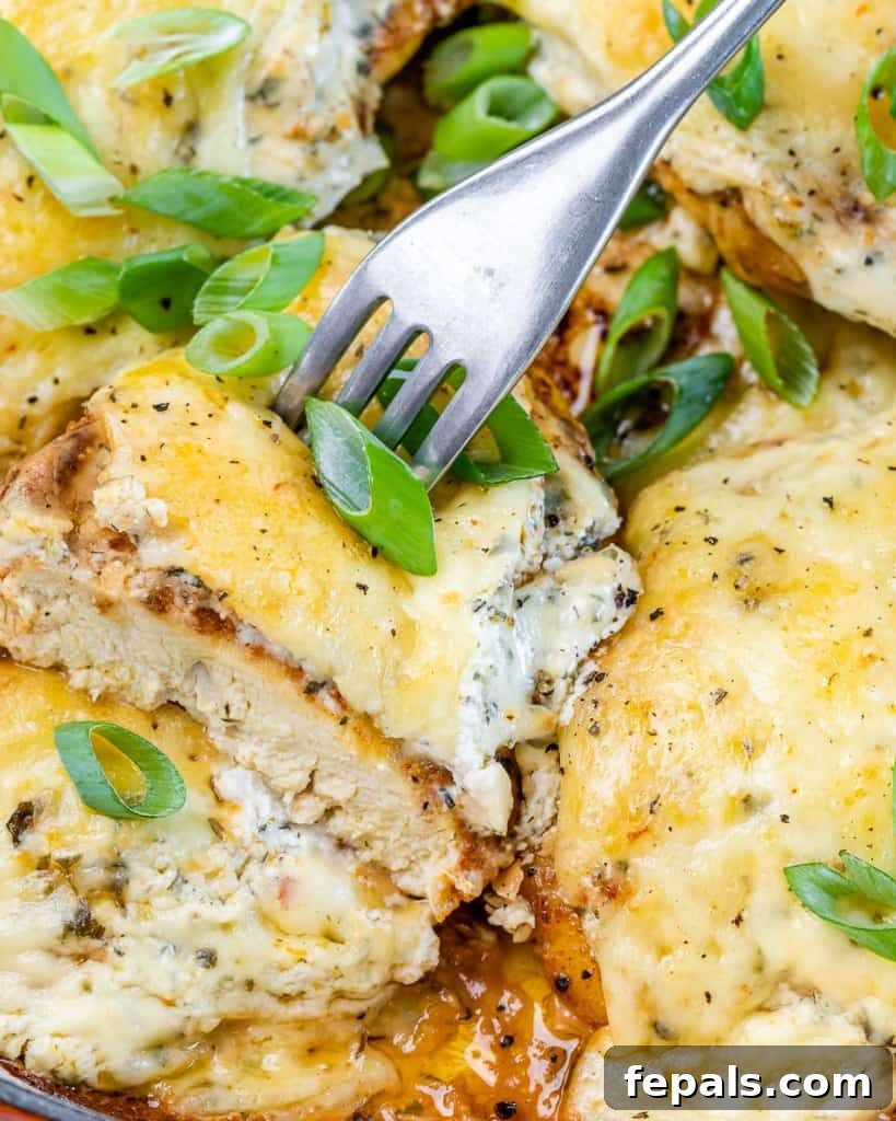 A fork stuck into a piece of cheesy chicken.
