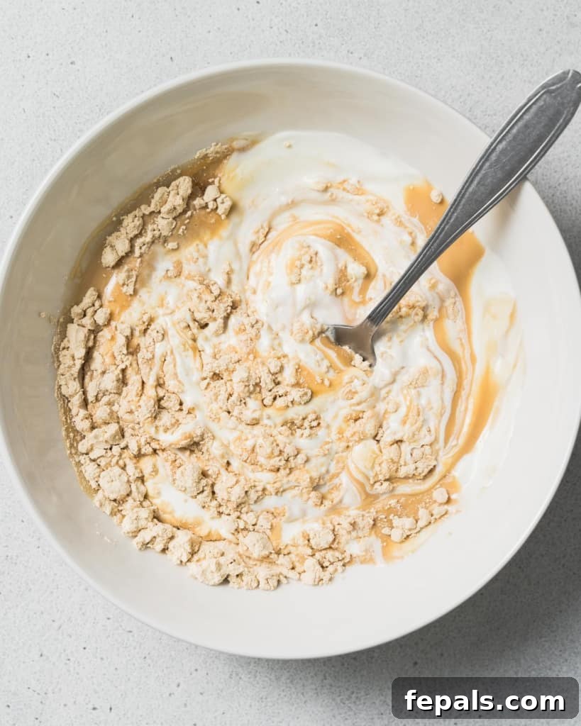 Peanut Butter Yogurt Frosty Bark 6 A hand stirring protein powder with yogurt and peanut butter in a bowl.