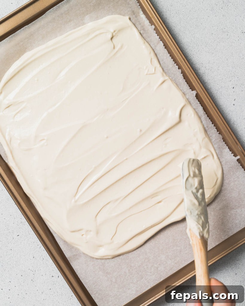 Peanut Butter Yogurt Frosty Bark 8 A spatula spreading the creamy yogurt mixture evenly on a parchment-lined pan.