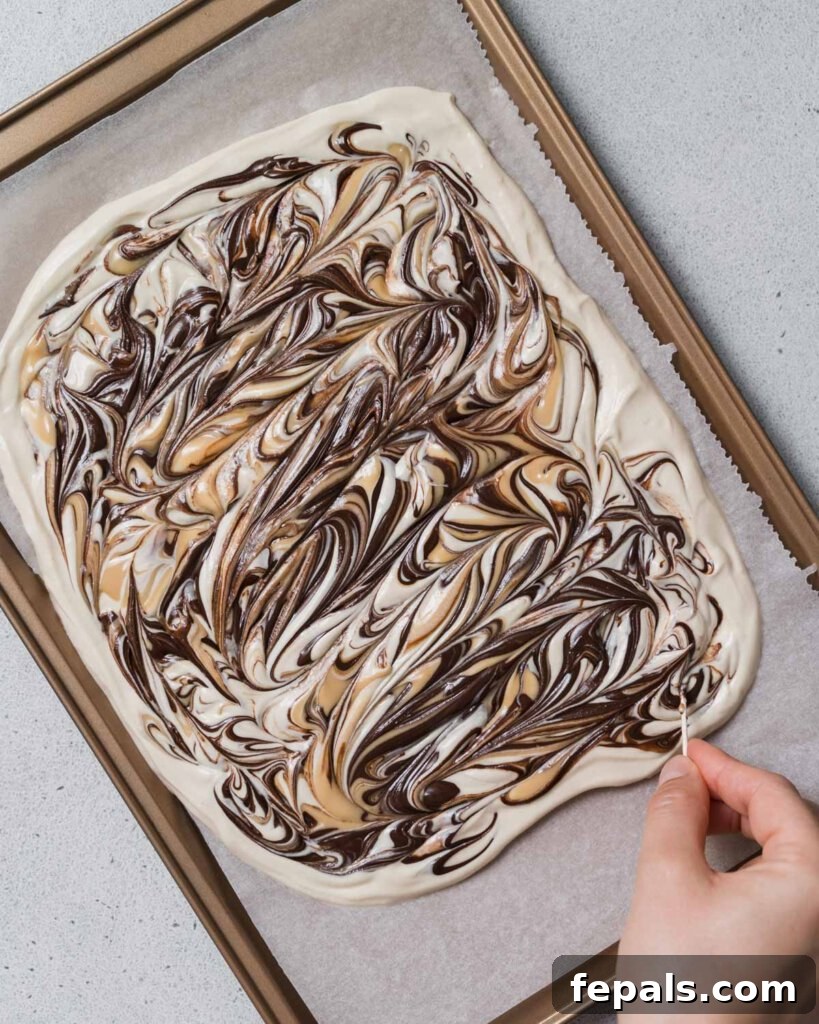 Peanut Butter Yogurt Frosty Bark 10 A toothpick being used to create intricate swirls with melted chocolate and peanut butter on the yogurt surface.