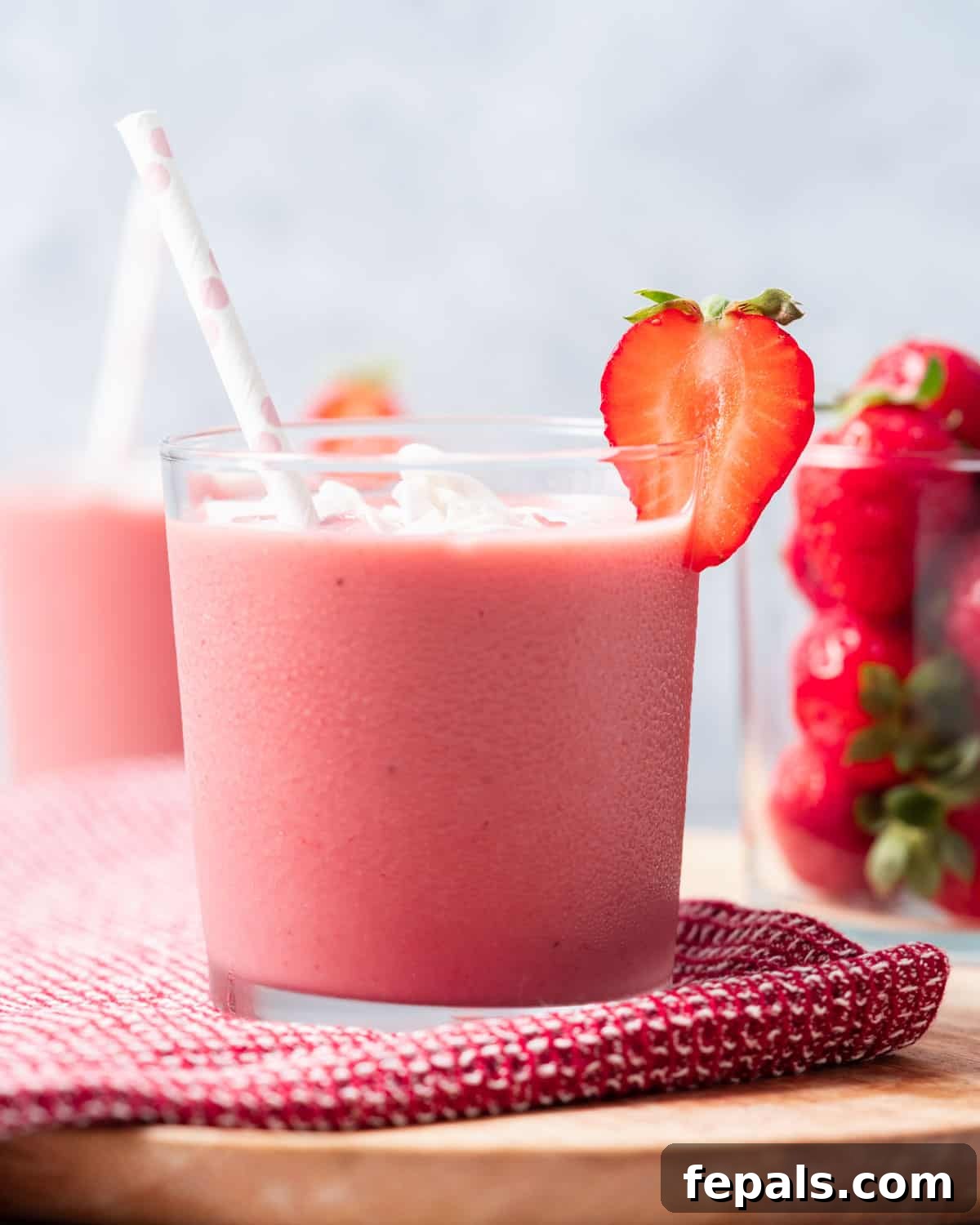 Side shot of strawberry banana smoothie in a glass with a straw, garnished with a fresh strawberry.