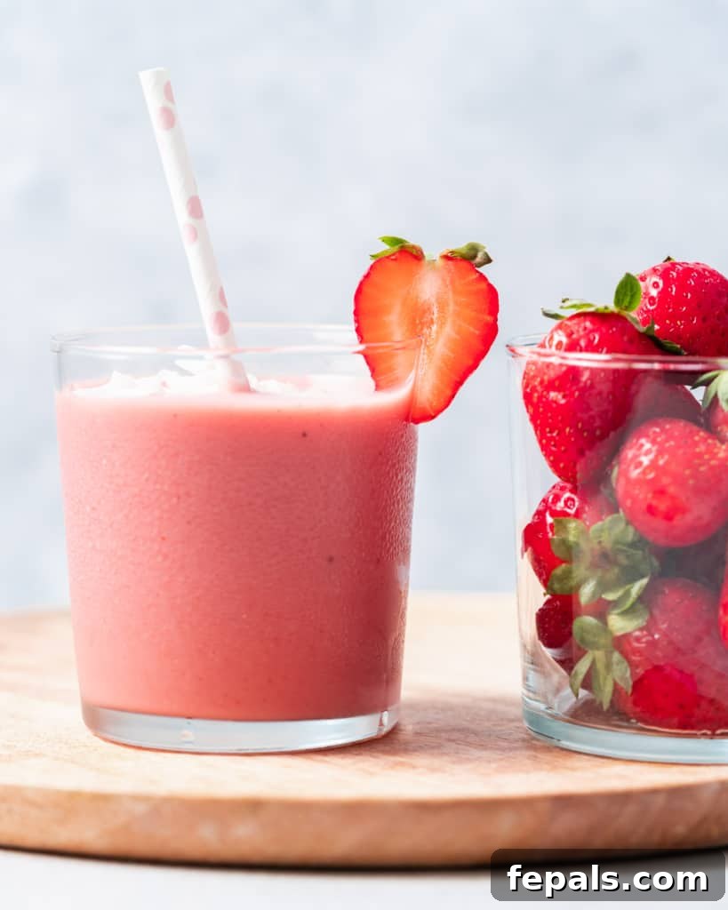 Side shot of strawberry smoothie in a cup with straw in cup, showing appealing texture.