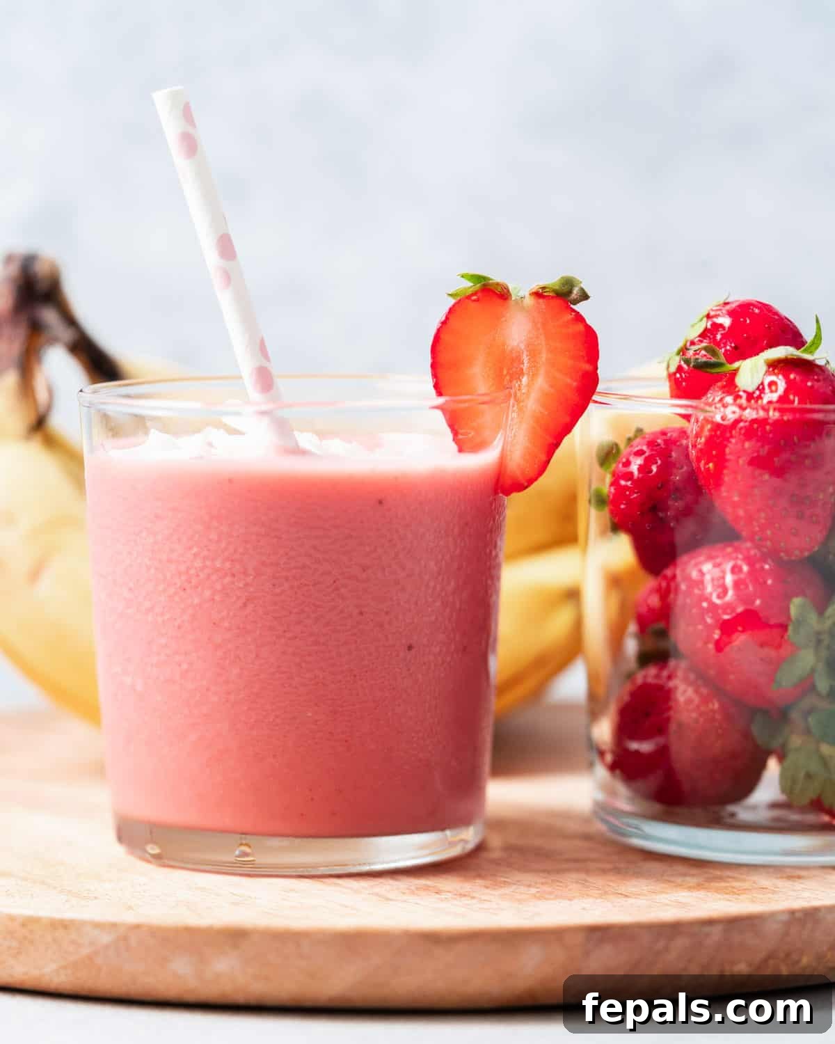 Strawberry banana smoothie in a glass near fresh strawberries and bananas, showcasing fresh ingredients.