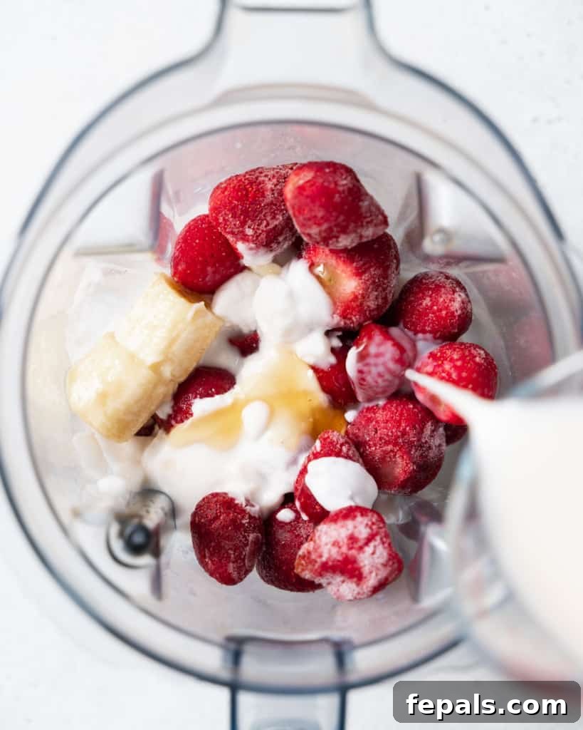 Pouring milk into a blender with frozen fruit – showing the first step of blending.