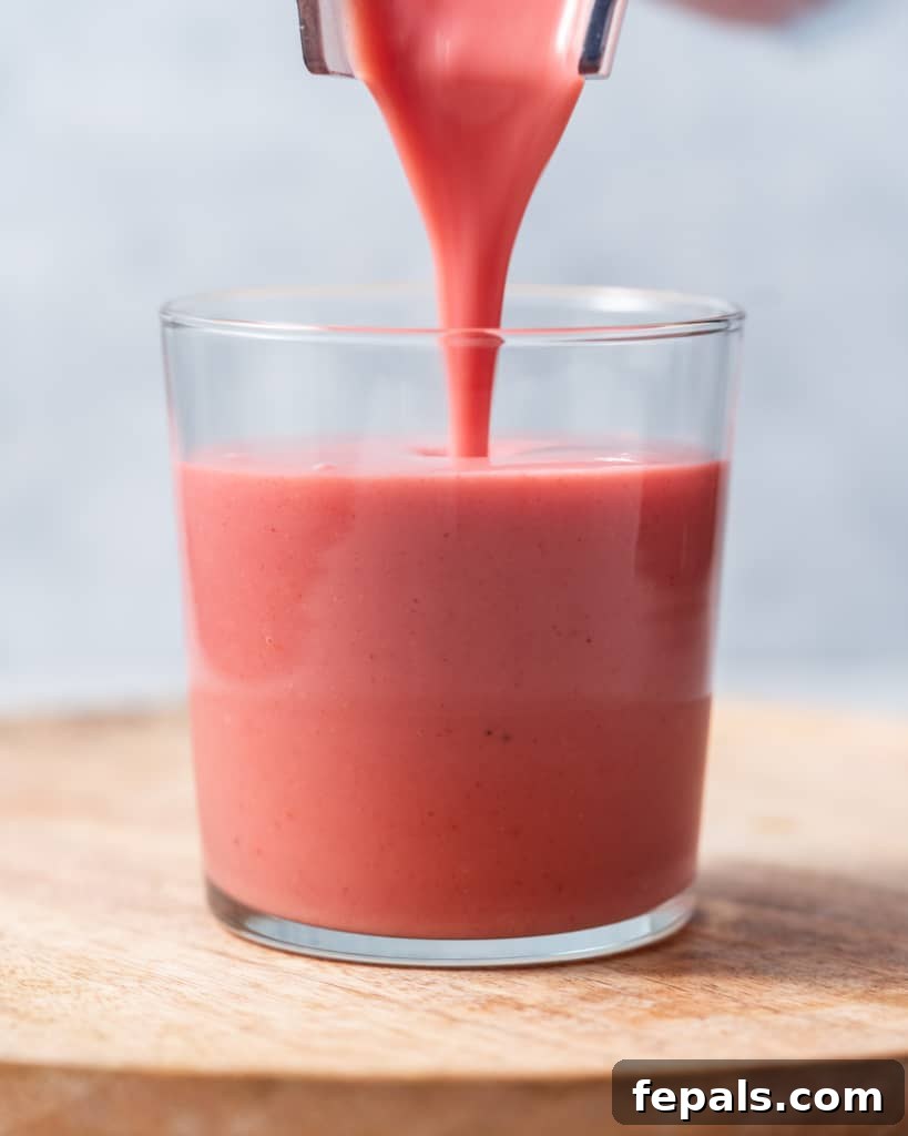 Pouring a strawberry smoothie into a glass – illustrating the serving step.