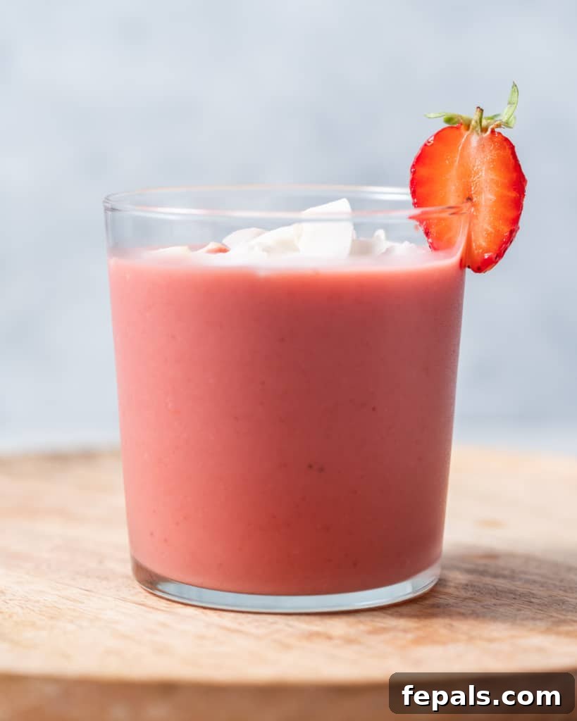 Smoothie in a glass garnished with coconut flakes and a fresh strawberry, ready to drink.