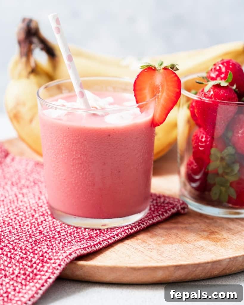 Side shot of a cup of pink strawberry banana smoothie with a straw in the cup.