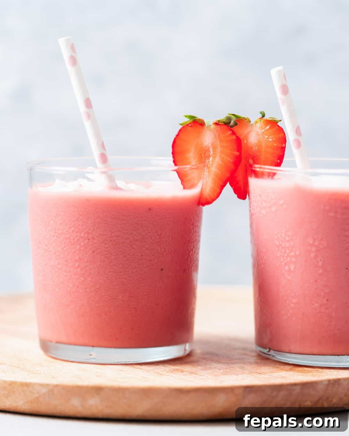 Two strawberry banana smoothies garnished with fresh strawberries, ready to serve.