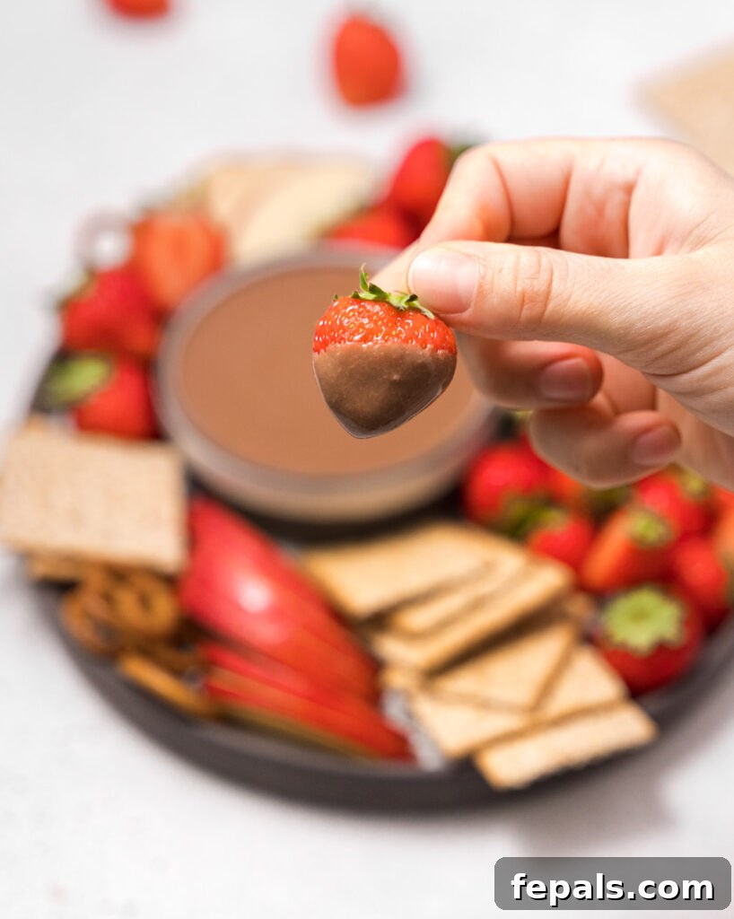 Hand holding a strawberry covered with chocolate dip, highlighting the appealing consistency.
