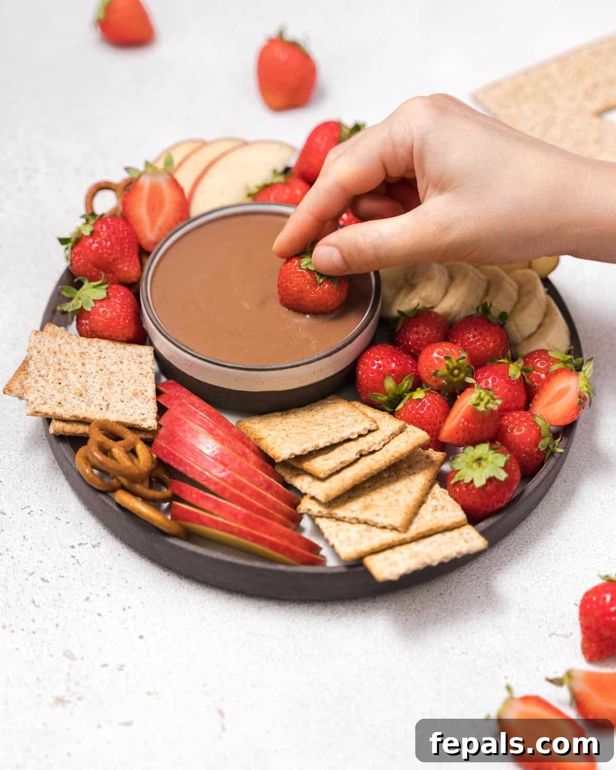 Hand dipping a ripe red strawberry into the smooth, rich chocolate fruit dip, highlighting the perfect pairing.