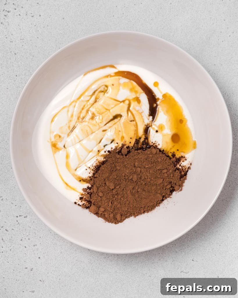 Adding yogurt, cocoa powder, and maple syrup to a mixing bowl, illustrating the initial step.