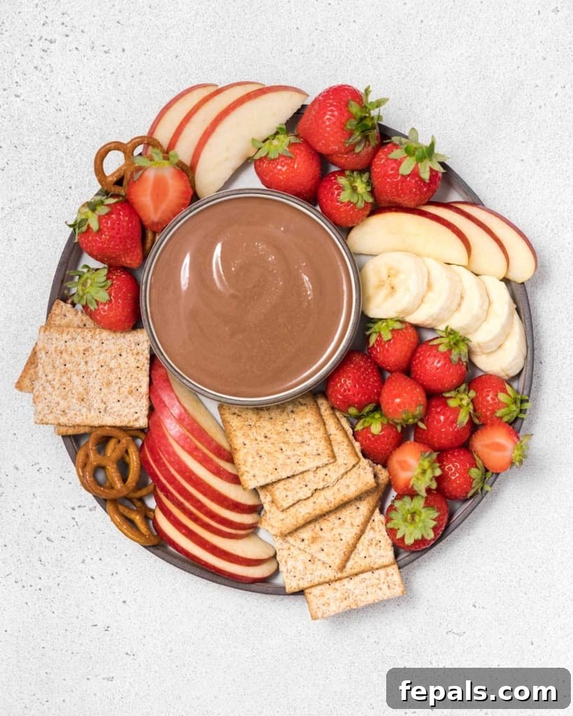 Finished chocolate dip served with an inviting array of apple slices, strawberries, pretzels, and crackers for dipping.