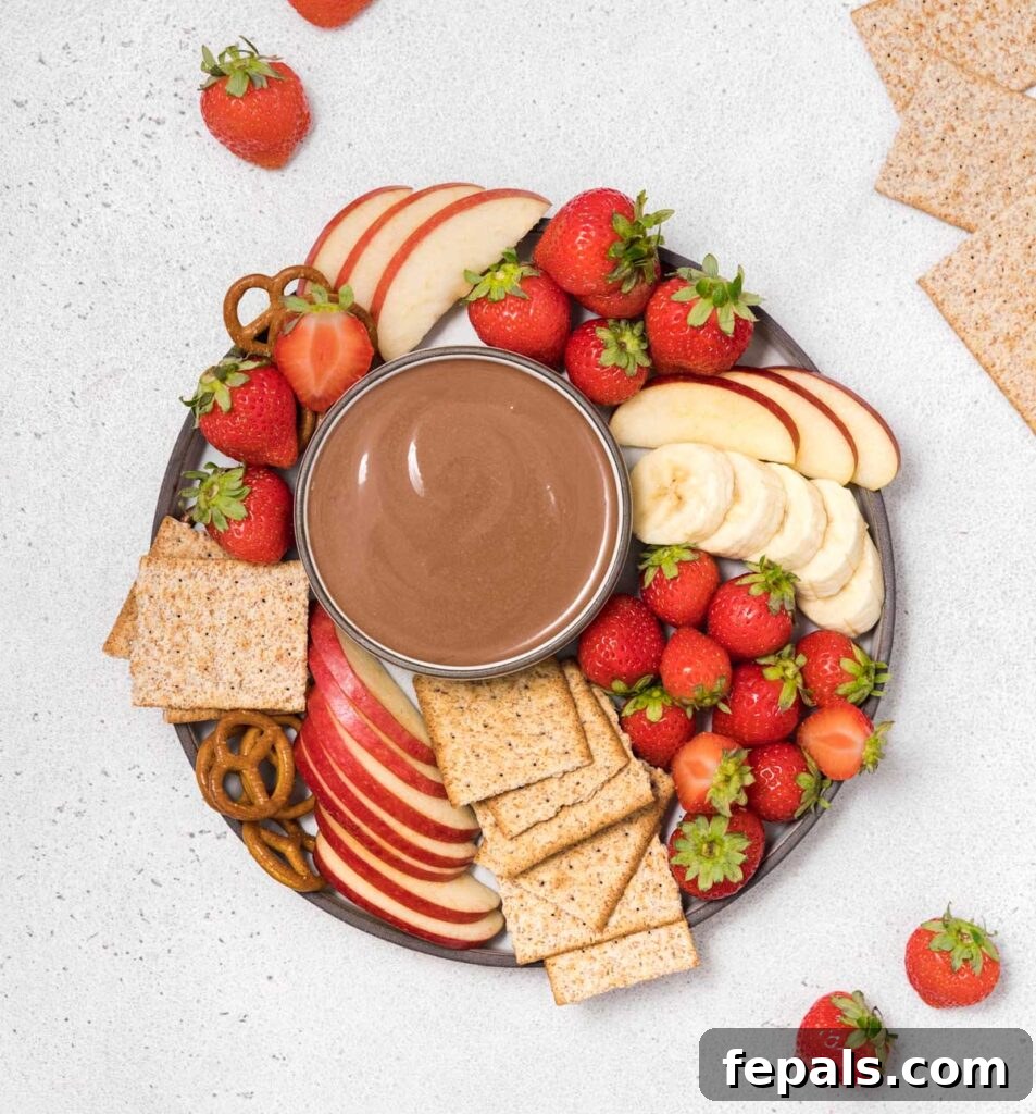 Top view of chocolate fruit dip over a plate with various fruits and crackers, presented attractively.