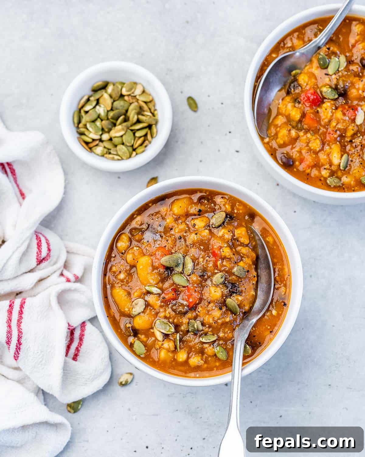 A top-down view of a round white bowl filled with vibrant Turkey Pumpkin Chili, with a spoon resting in the bowl, garnished with fresh herbs or seeds.