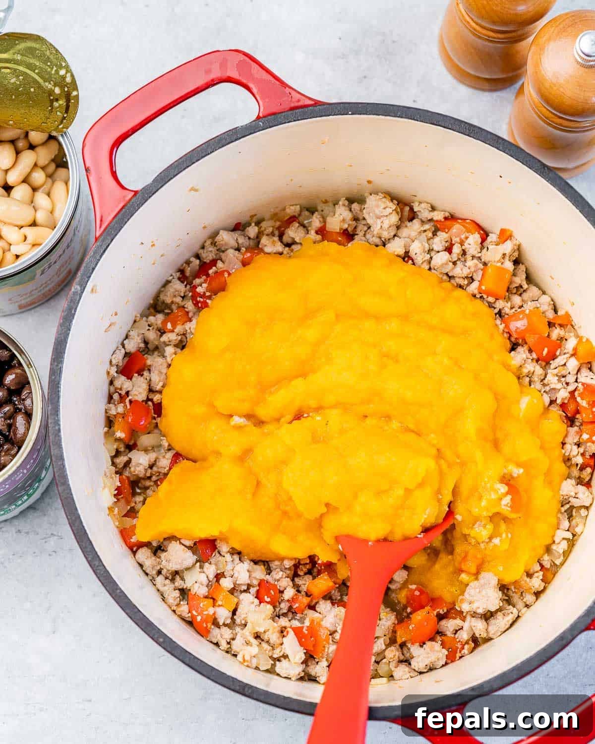 Adding smooth pumpkin puree to the pot containing sautéed vegetables and cooked ground turkey.