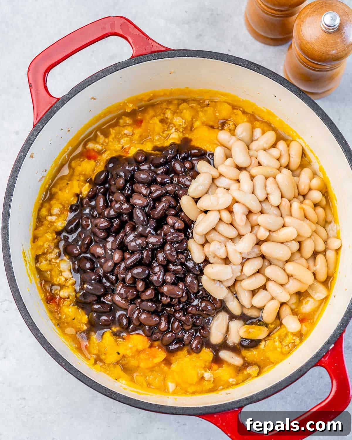 Adding rinsed black and white beans into the simmering pumpkin chili in a Dutch oven.