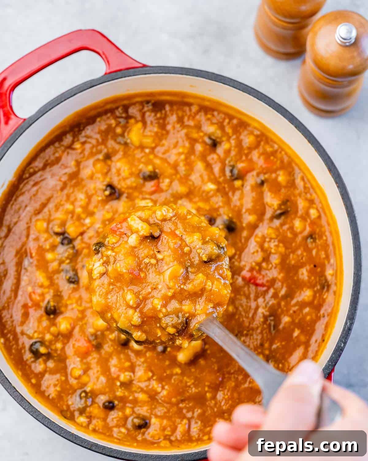 A ladle carefully scooping out a generous portion of rich, orange-hued chili from a large pot.