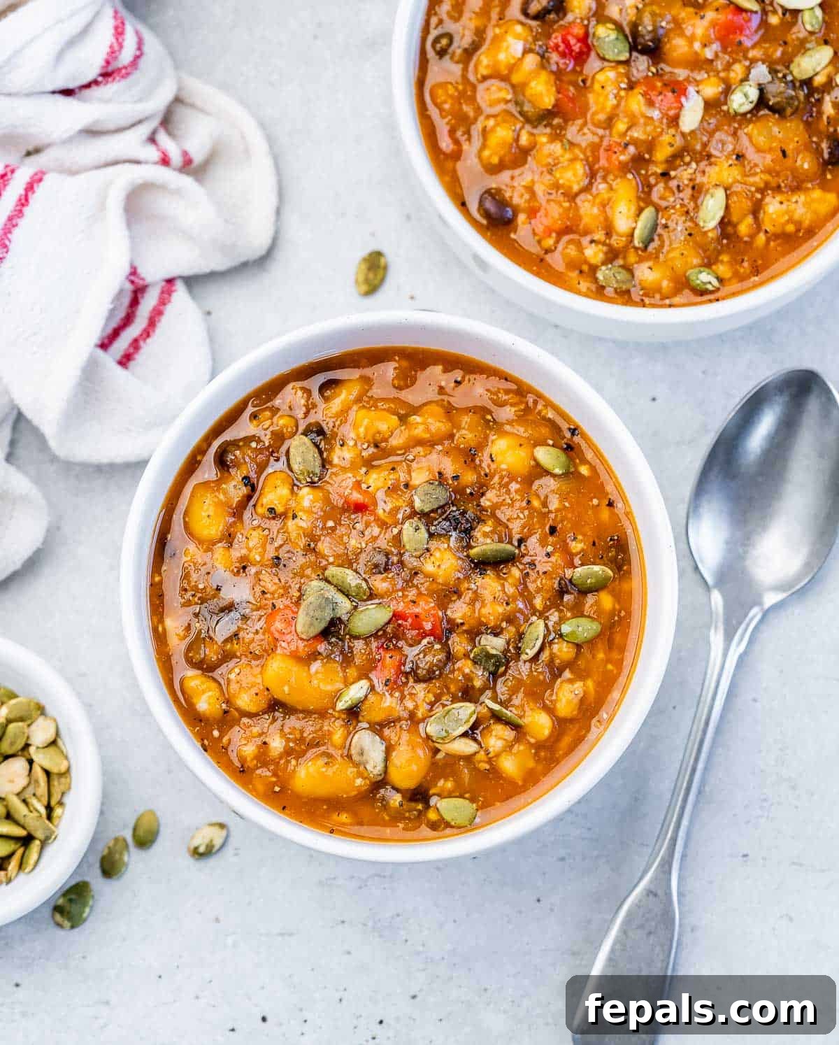 Two pristine white bowls filled with steaming Turkey Pumpkin Chili, garnished and ready to be enjoyed.