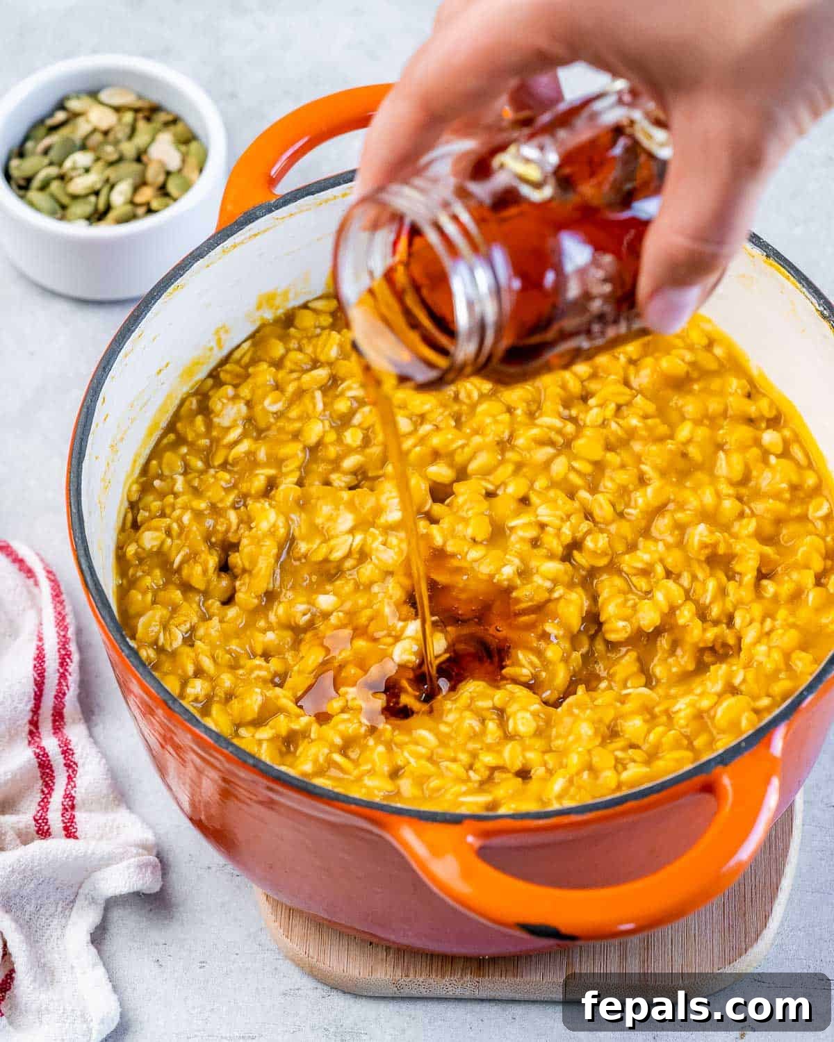 Adding maple syrup to cooked pumpkin oats in a pot.